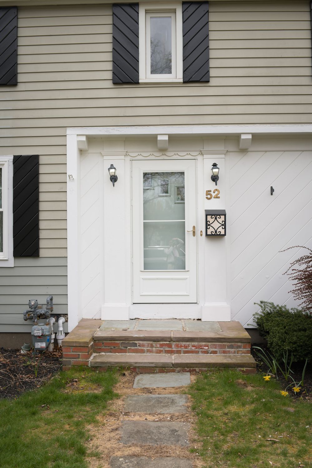 Colonial-style home entrance with white door, brick steps, and house number 52.