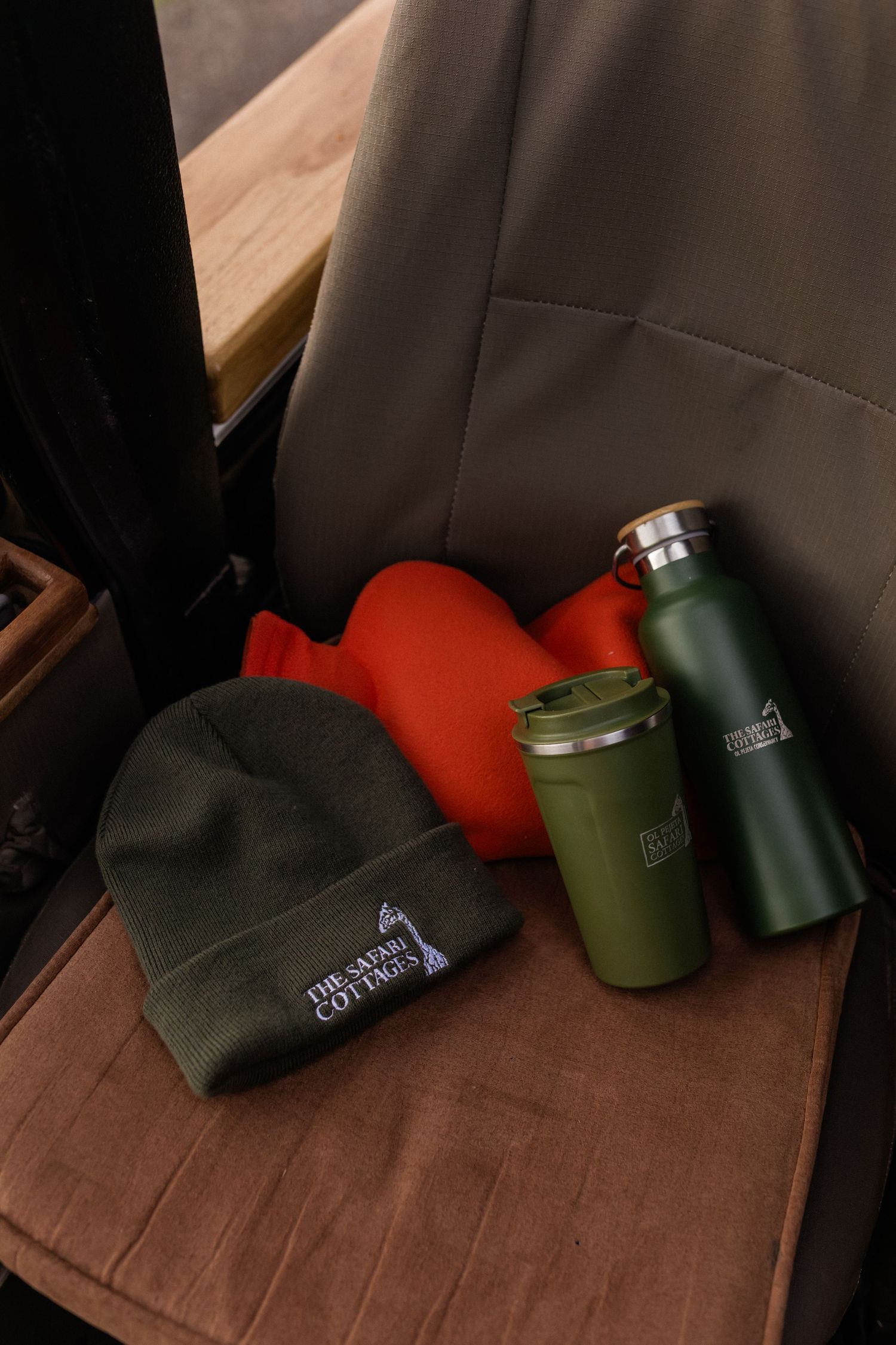 Green beanie hat, travel mug, water bottle, and red hot water bottle on a brown seat at The Safari Cottages.