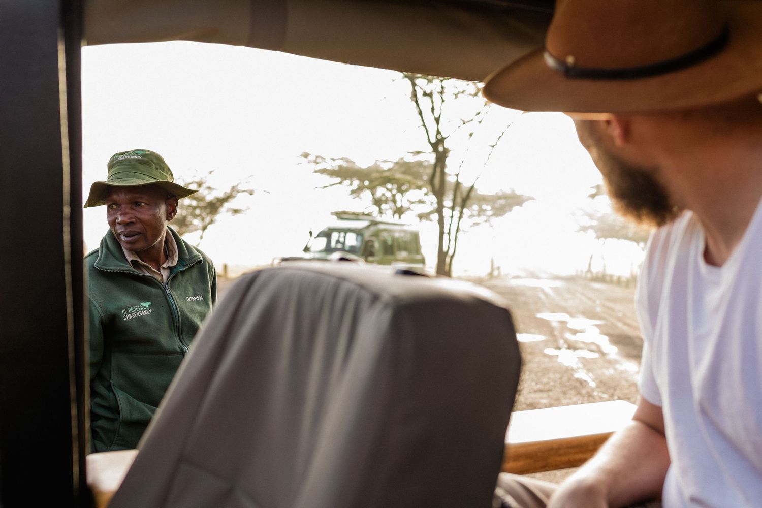 Safari guide speaking to tourist through vehicle window in African savanna landscape.