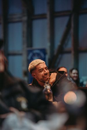 Smiling man with blonde hair at an indoor event surrounded by a crowd of people.