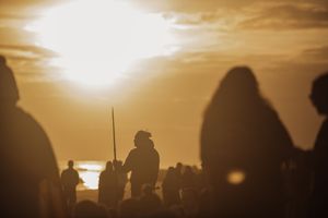 Silhouettes of people gathered at sunset, with a figure holding a spear against a glowing golden sky.