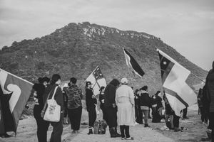 Black and white photo of people holding flags near a rocky hill during an outdoor gathering or protest.