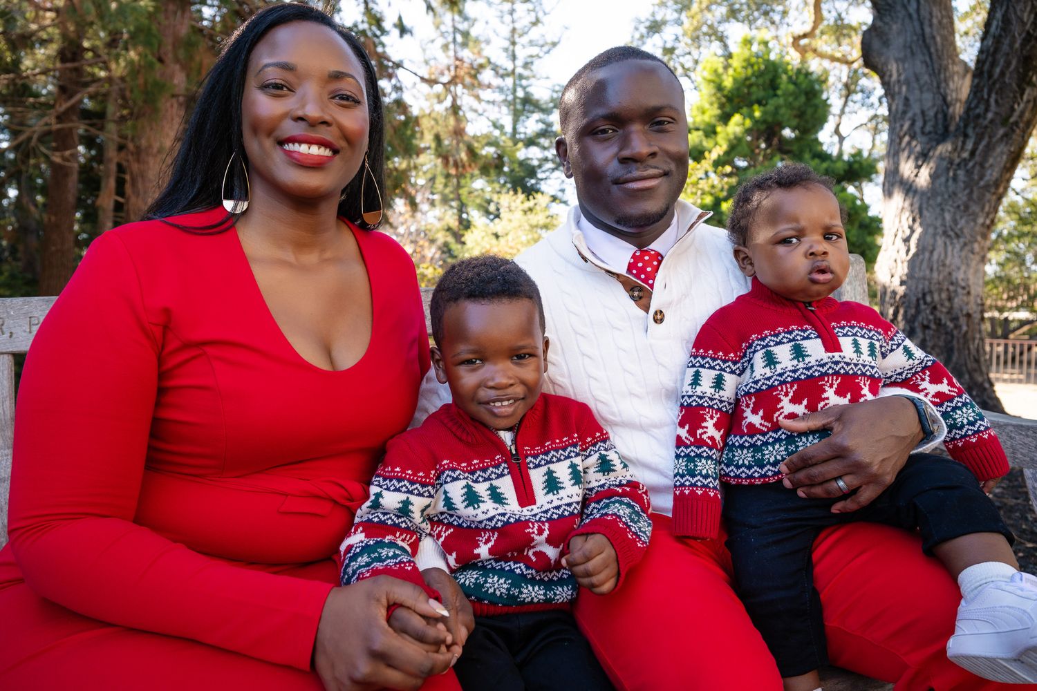Family of four in matching Christmas sweaters posing outdoors for a festive holiday portrait photo.