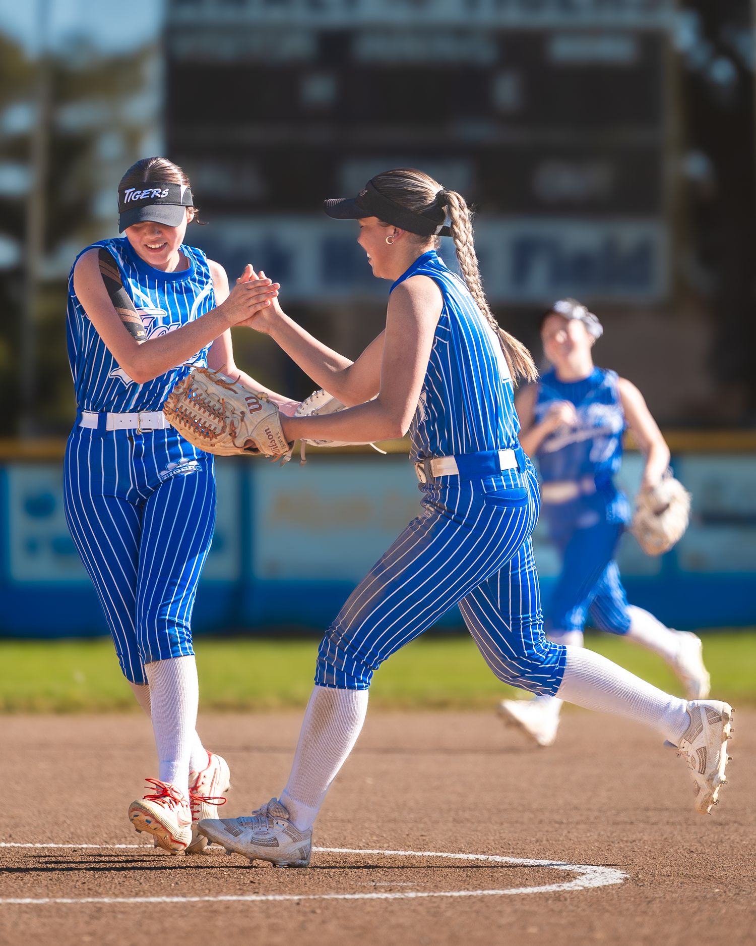 Two softball players in blue uniforms celebrate on the field during a game.