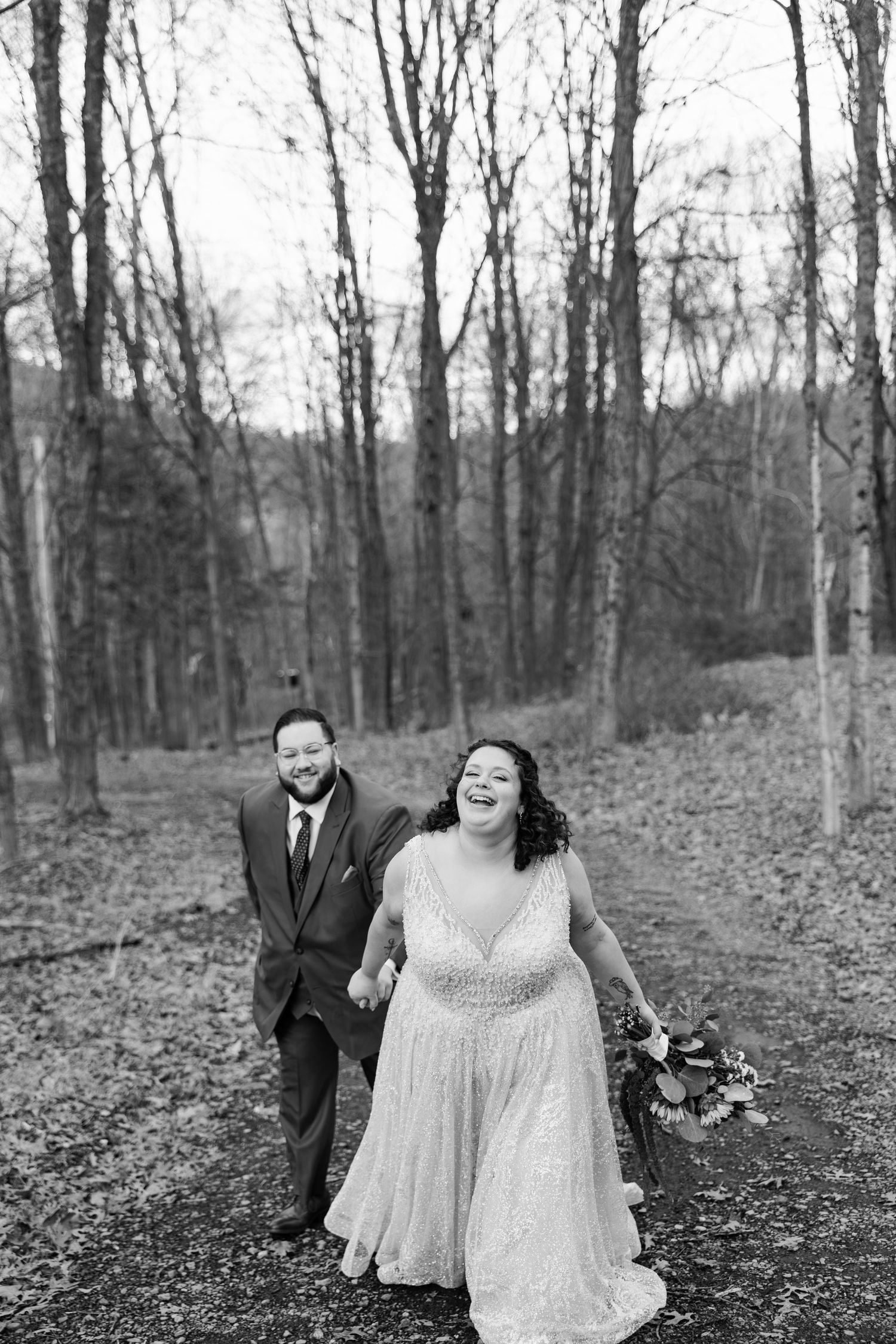Joyful bride and groom laughing together outdoors, bride wearing veil and strapless gown, groom in black tuxedo.