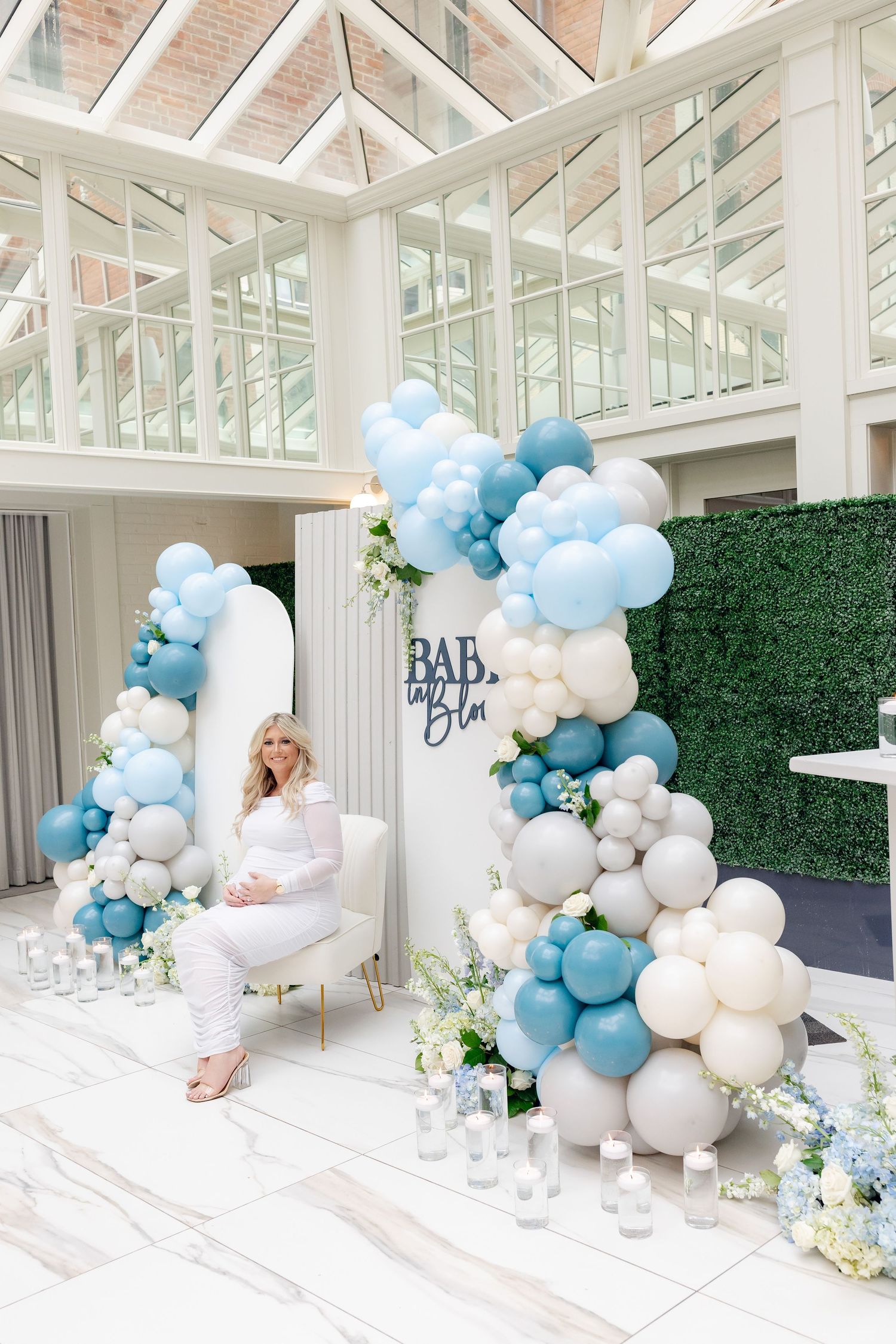 Elegant baby shower venue with blue and white balloon arch, floral decor, and Baby Bloom signage.