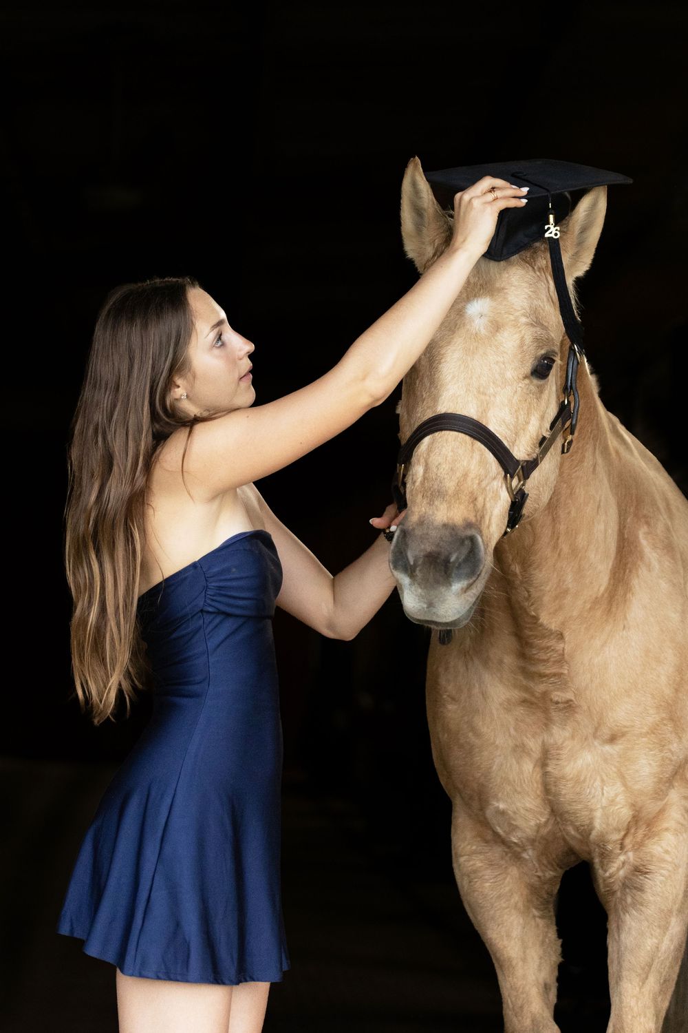 girl putting her graduation cap on her horse