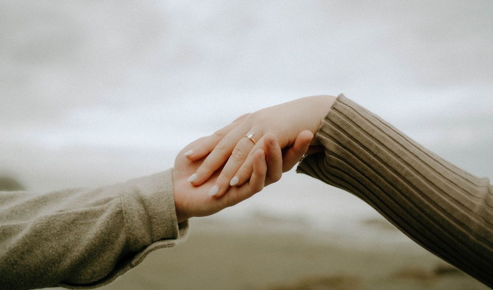 Two hands gently touching, one wearing an engagement ring, symbolizing love and connection against a soft blurred background.