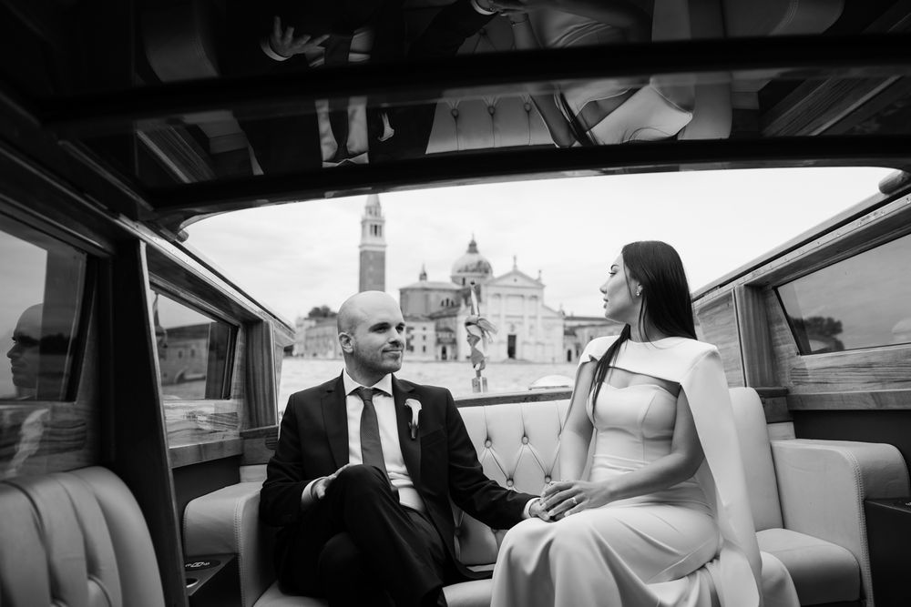 Bride and groom sitting together in a vintage car boat in Venice, Italy, with San Giorgio Maggiore church in the background.