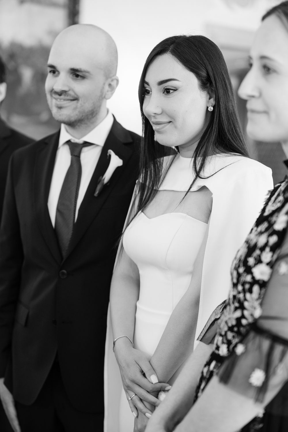 Black and white photo of a smiling bride in white dress and groom in dark suit at their wedding ceremony.