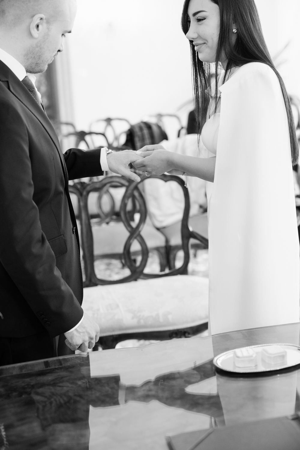 Black and white photo of bride placing wedding ring on groom's finger during ceremony.