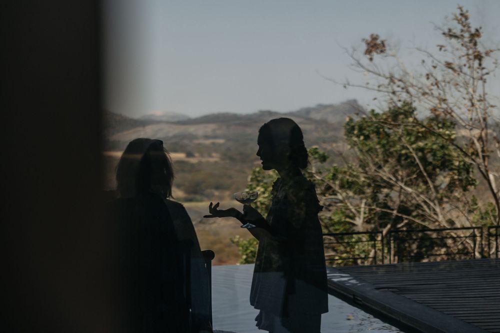 Two silhouetted women conversing outdoors with scenic mountain landscape and trees in background.