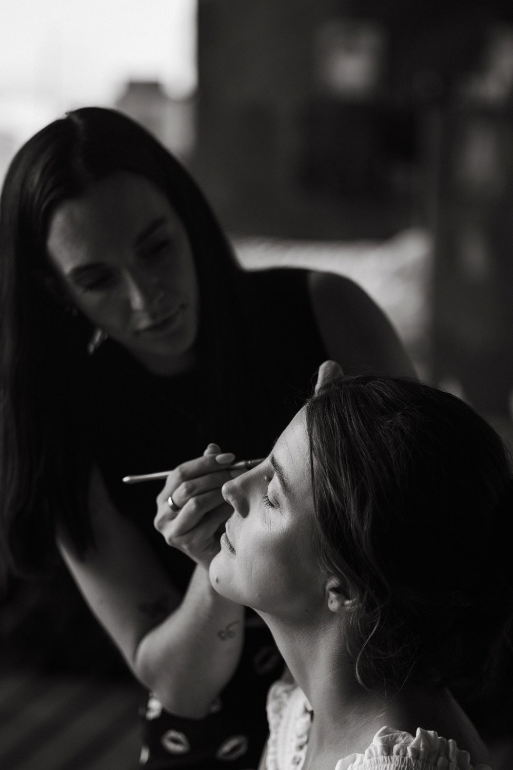 Black and white photo of a makeup artist applying eyeshadow to a bride before her wedding ceremony.