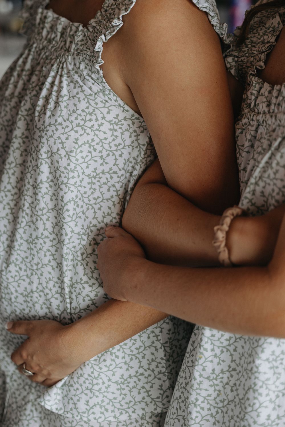 Two girls in matching floral sundresses share a warm embrace, showcasing coordinating outfits.