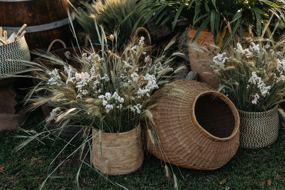 Rustic wicker baskets and dried wildflower arrangements on grass, boho outdoor wedding decor with wheat and white blooms.