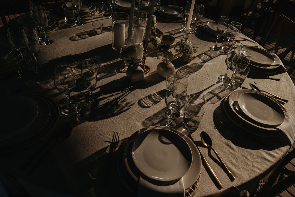 Elegant dark-toned round dining table set with charger plates, crystal glassware, candles, and black cutlery for a formal event.
