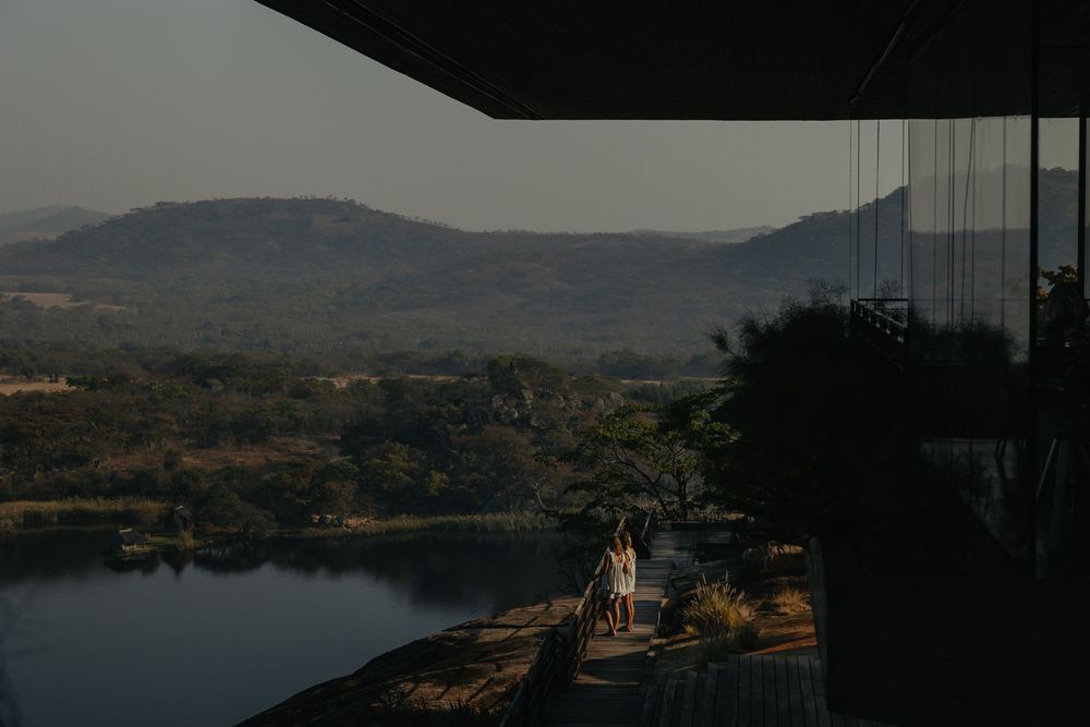 A couple walks along a scenic overlook with sweeping mountain and lake views.