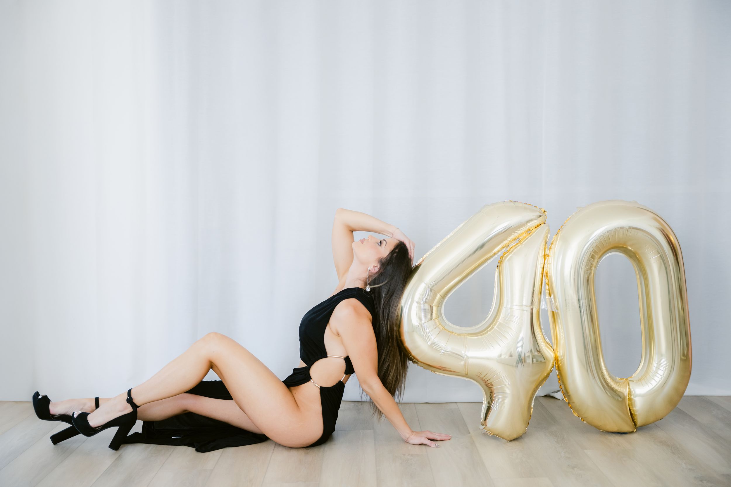 Woman in black outfit posing beside gold number 40 balloons celebrating a 40th birthday milestone.