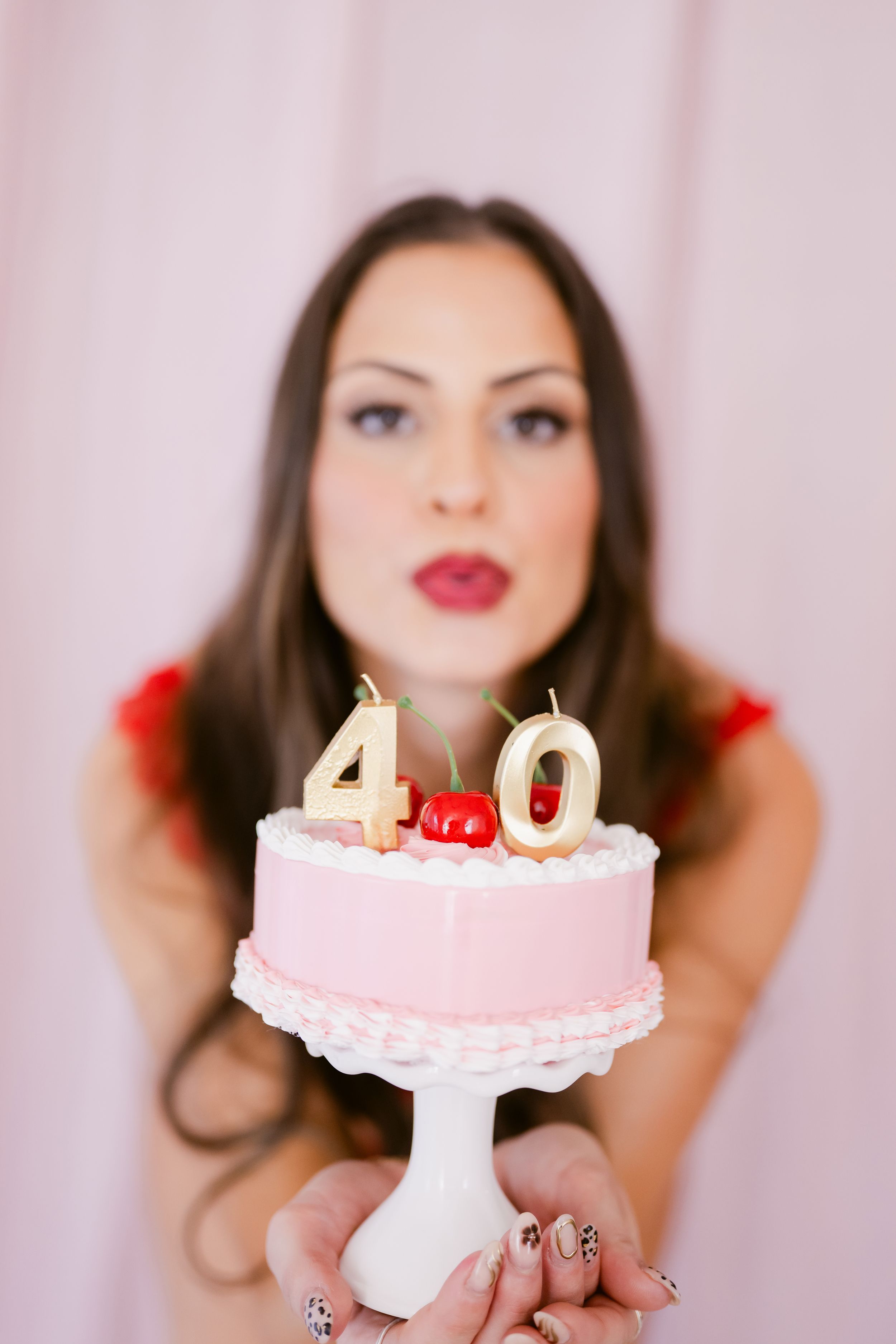 Woman holding a pink 40th birthday cake with gold candles and cherries on top.