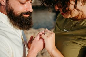 Bearded man placing an engagement ring on a woman's finger during a romantic outdoor proposal.