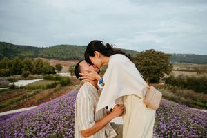 Couple sharing a romantic kiss in a vibrant purple flower field with lush green hills in the background.