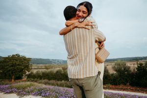 Couple embracing and smiling in a scenic lavender field with rolling hills in the background.