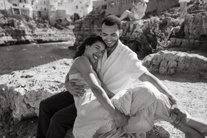 Black and white photo of a happy couple embracing on rocky coastal cliffs in a scenic Mediterranean town.