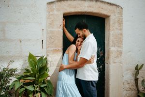 Happy couple hugging and laughing by a rustic green door with lush plants in a charming village.
