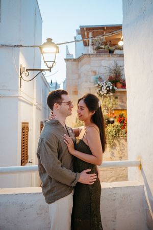 Romantic couple embracing and smiling at each other in a charming whitewashed Mediterranean alley at golden hour.