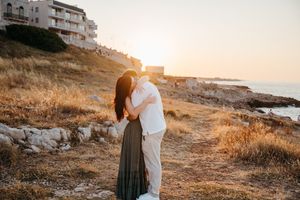 Couple sharing a tender embrace at sunset on a rocky coastal landscape with the sea in the background.
