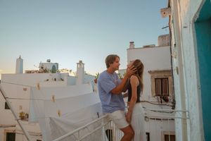 Romantic couple embracing on a rooftop terrace with white Mediterranean buildings and clear blue sky backdrop.