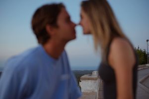 Couple sharing a romantic kiss outdoors at dusk with scenic landscape in background.