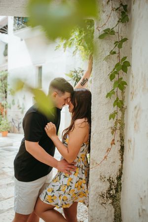 Romantic couple embracing and almost kissing against a rustic white wall with ivy, surrounded by lush greenery.