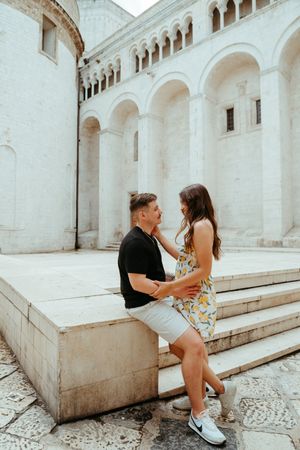 Romantic couple sharing an intimate moment on steps of a historic white stone cathedral.