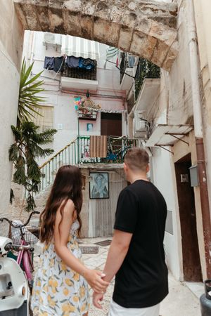 Couple holding hands exploring a charming narrow alleyway with stone arch in an old Italian town.