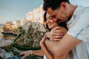 Romantic couple embracing on a balcony overlooking a scenic coastal Italian cliffside town.