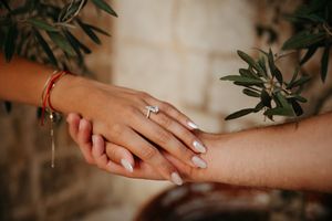 Close-up of elegant engagement ring on bride's hand with olive branch background.