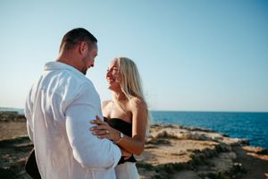 Couple dancing romantically on rocky coastal cliffs overlooking a calm blue sea.