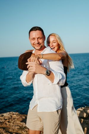 Happy couple hugging and laughing together on rocky shoreline with blue ocean in the background.