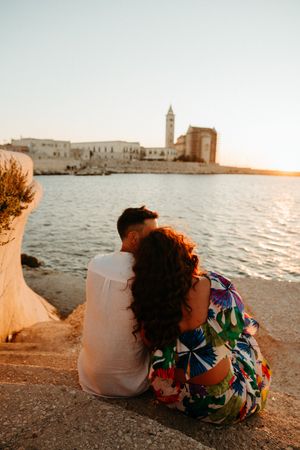 Romantic couple sitting together watching sunset over historic Italian coastal town.