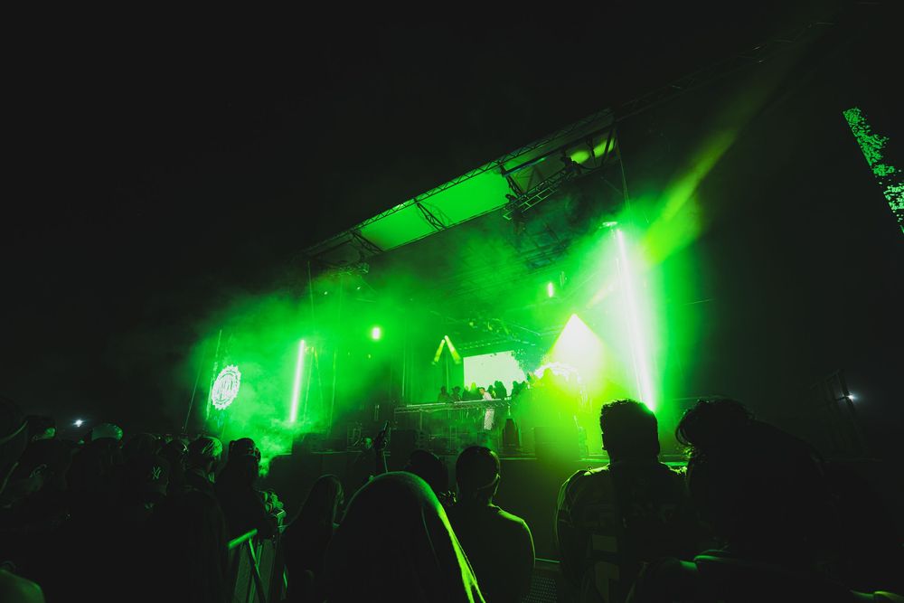 Crowd silhouettes at an outdoor music festival stage with dramatic green lighting at night.