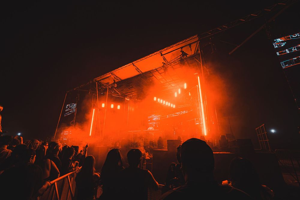 Outdoor music festival stage glowing with orange lights and smoke at night.