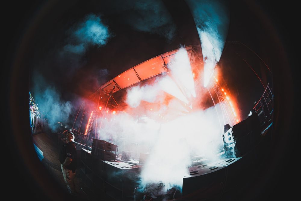 Fisheye view of a dramatic concert stage with blue and orange smoke effects under bright lights.