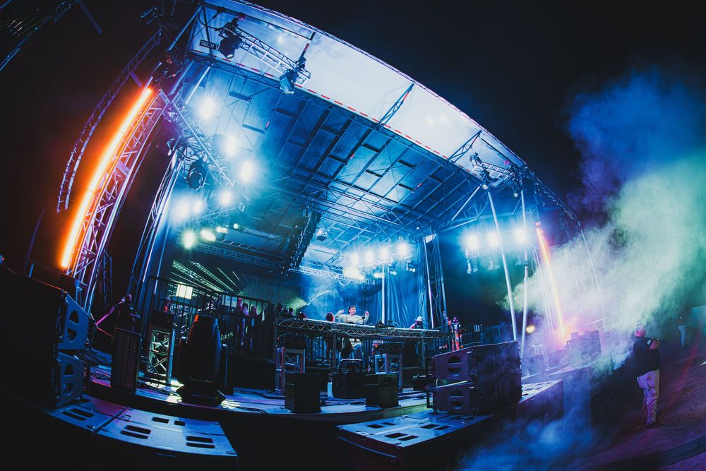 Vibrant concert stage with colorful lights, fog, and equipment setup at an outdoor music festival.