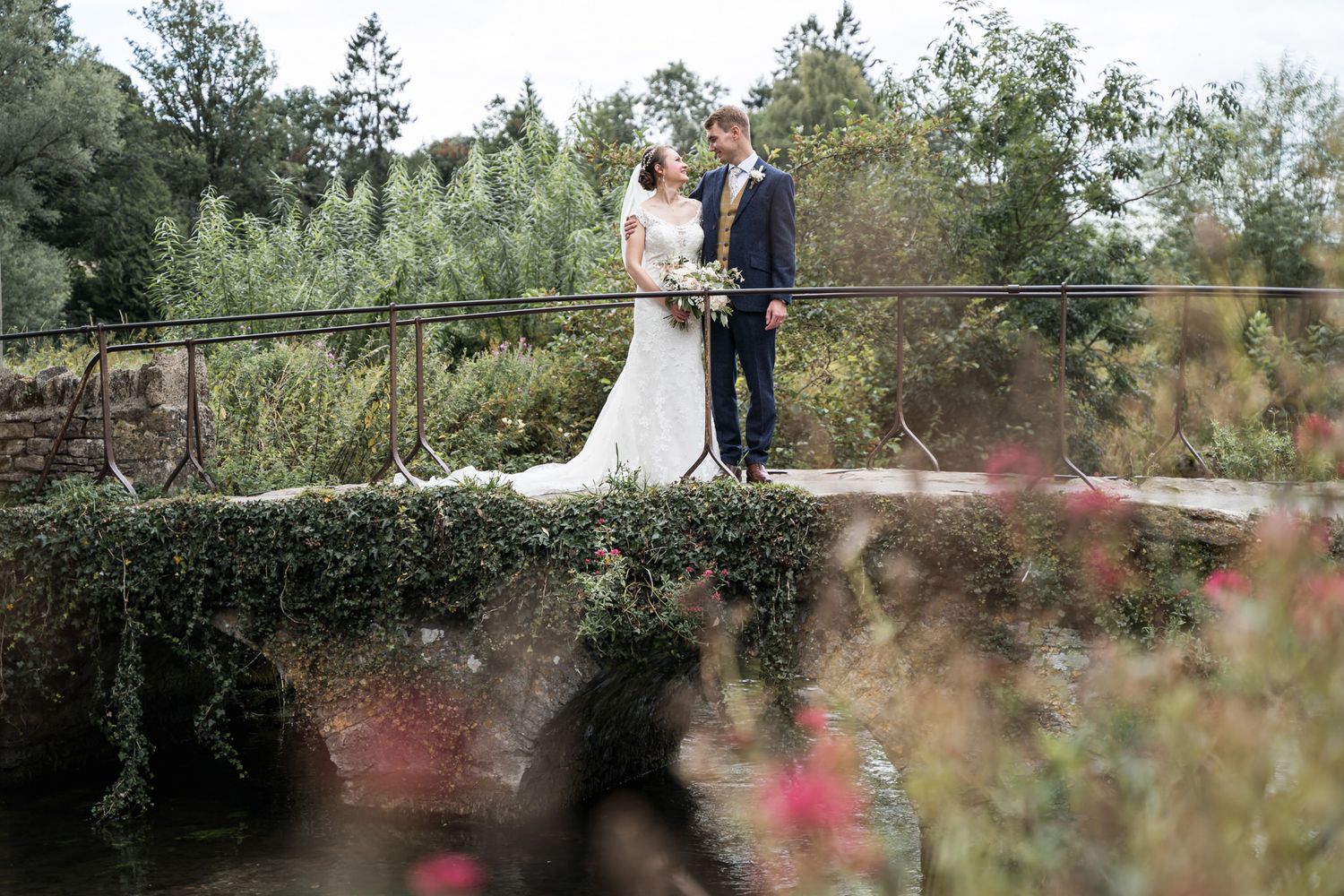 Bride and groom sharing a romantic moment on a moss-covered stone bridge in Bibury at their Swan Hotel Wedding