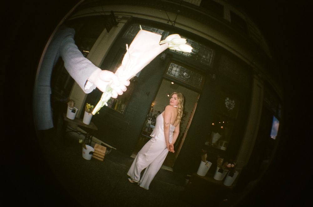 Woman in white dress standing in dark venue, fisheye lens perspective with arm reaching into frame.