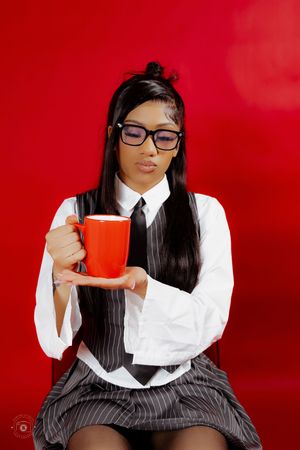 Young woman in school uniform holding a red coffee mug against a bold red background.