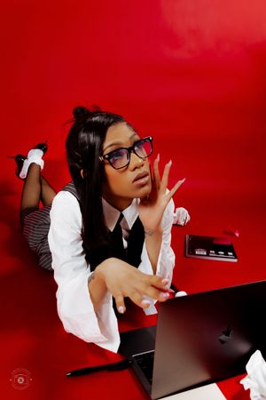 Young woman in glasses and school uniform poses with laptop against vibrant red background.