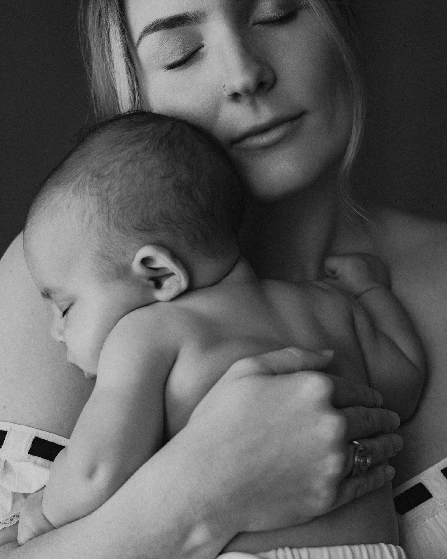Black and white photo of a mother tenderly holding her newborn baby close to her chest with eyes closed.