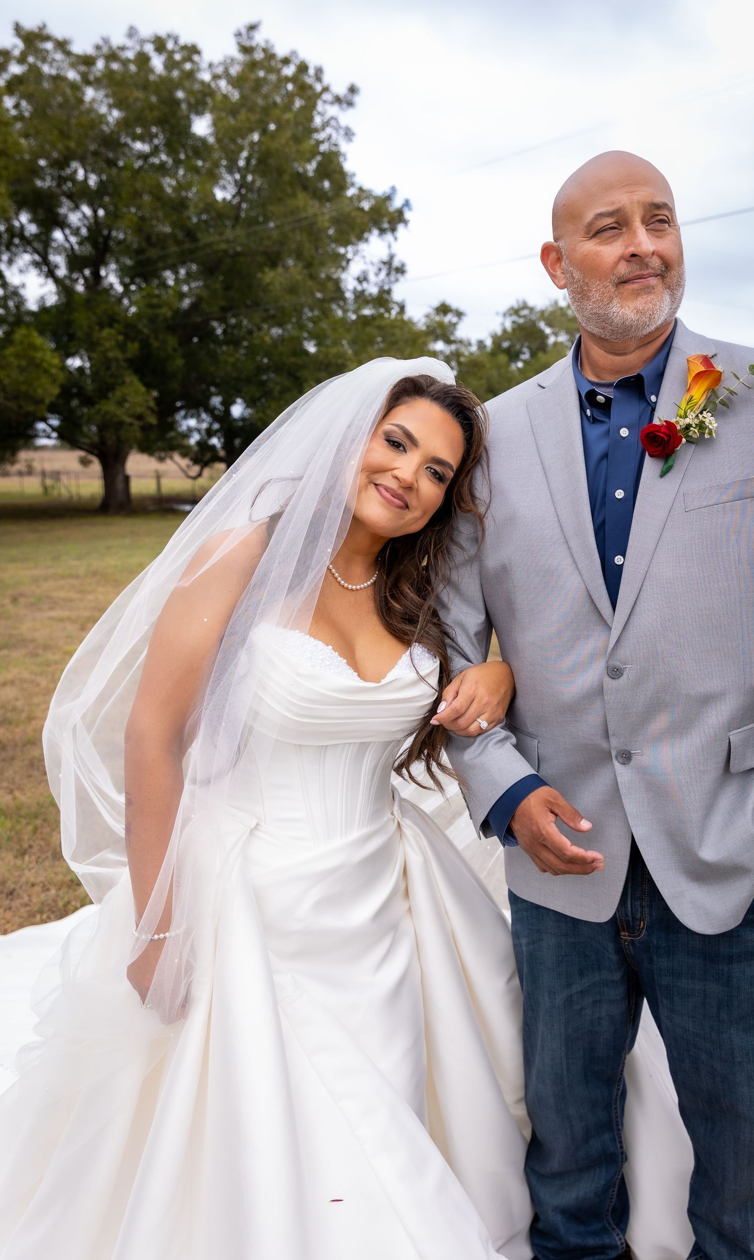 Young woman in a stunning teal and gold quinceañera ballgown with a large bow, posing in a lush garden setting.
